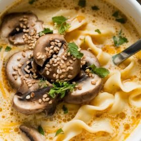 Bowl of creamy coconut curry ramen topped with fresh cilantro and lime wedges.